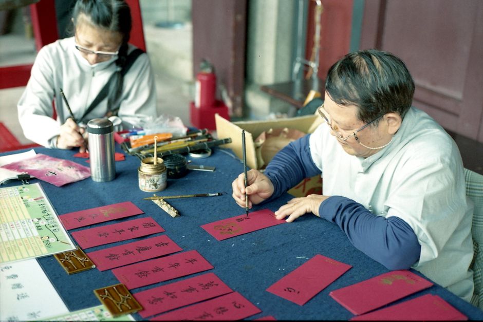 Elderly calligraphers in Taipei engage in traditional Chinese calligraphy, writing on red envelopes.