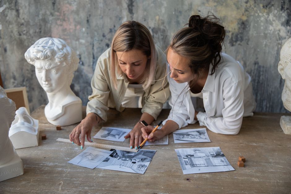 Two female artists working together, sketching with plaster busts on table.