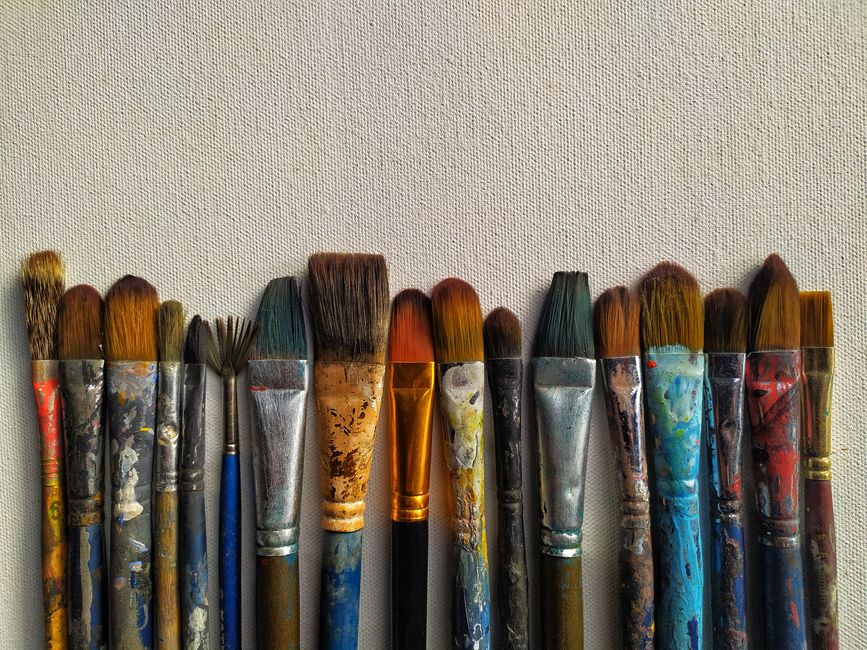 A collection of various paintbrushes aligned against a textured canvas surface.